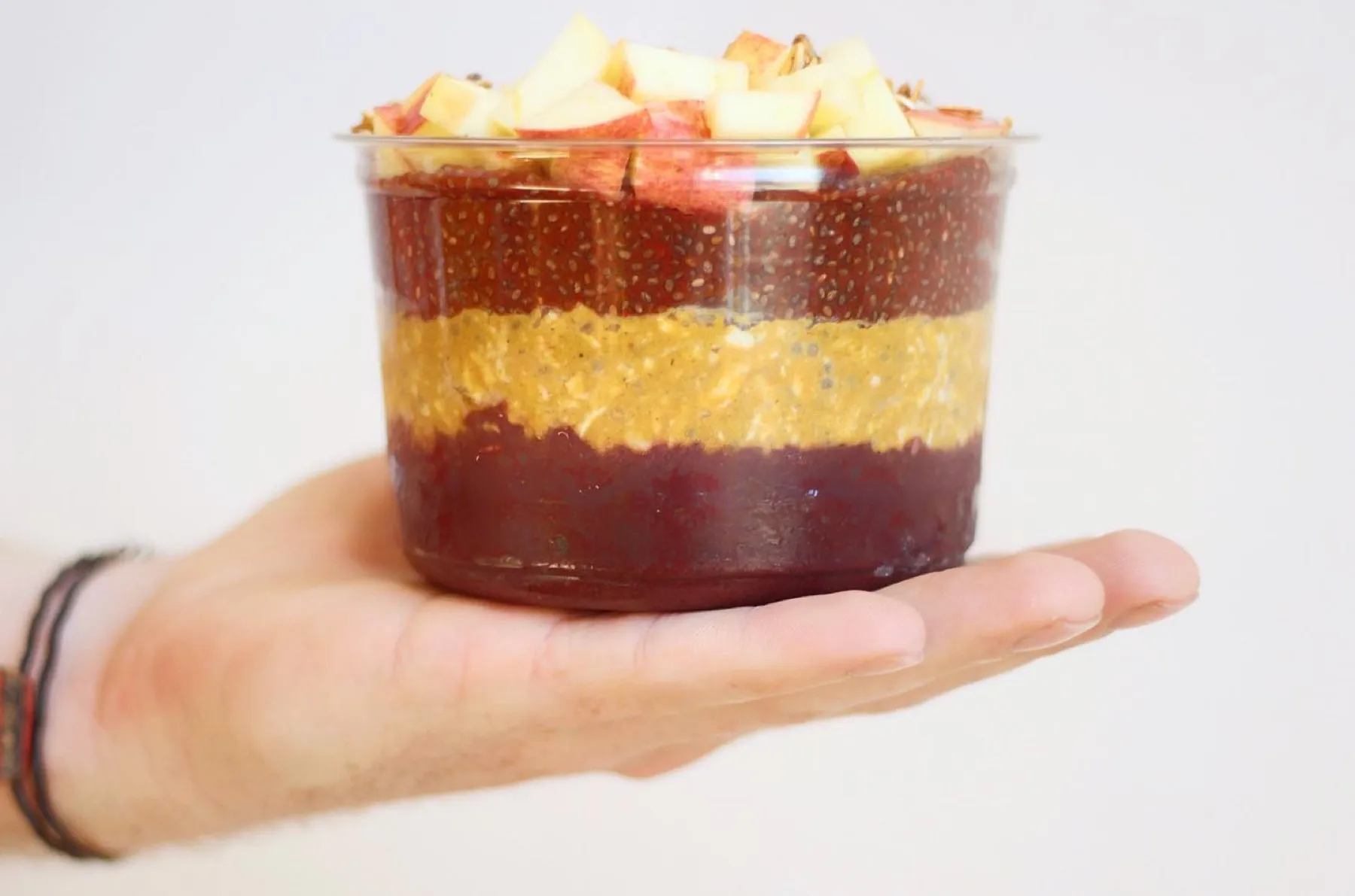 A hand holding a clear cup layered with dark berry pudding, golden chia and fresh fruit.