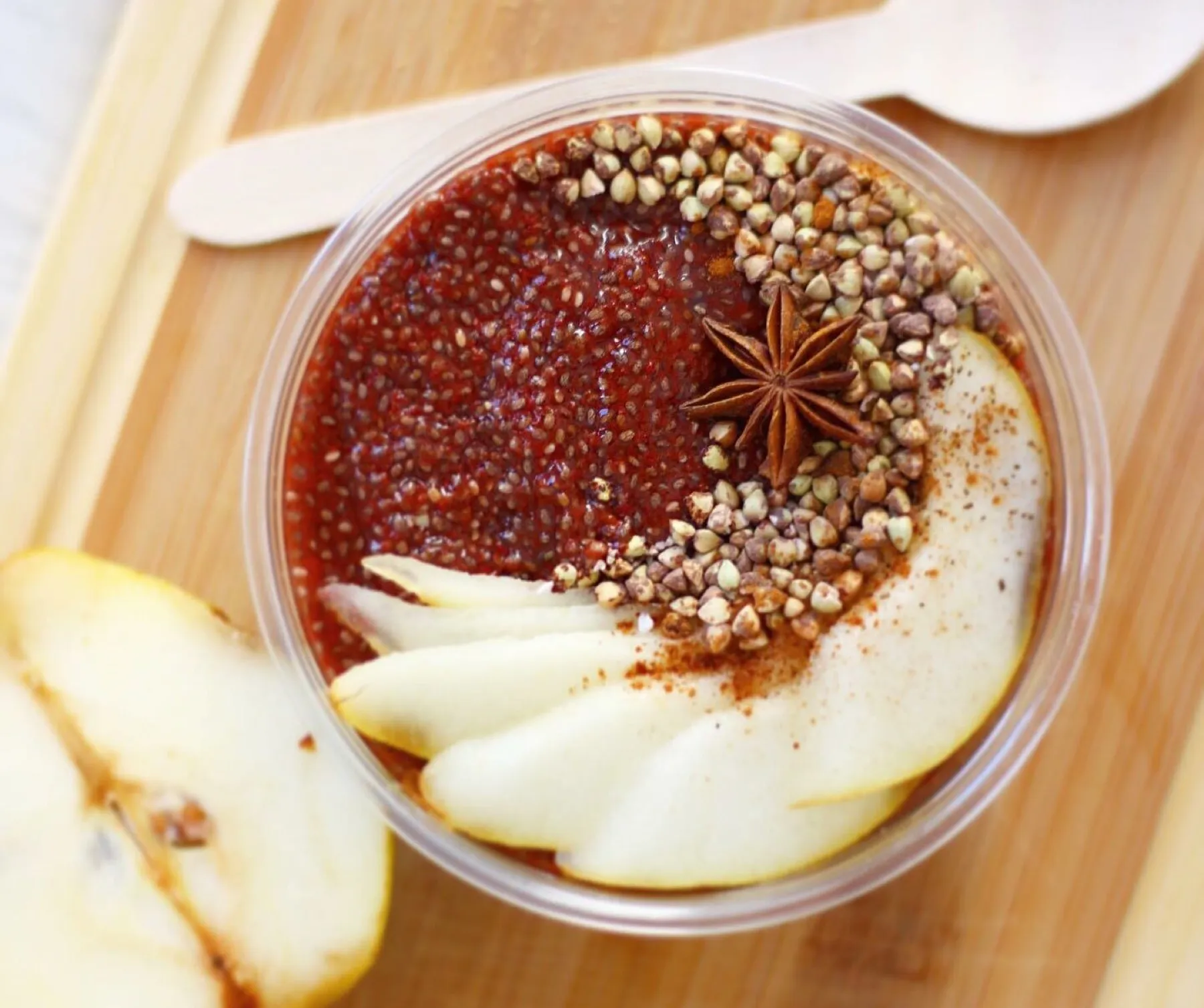 A bowl of red autumn berry chia pudding topped with sliced pear, star anise and pink peppercorns.