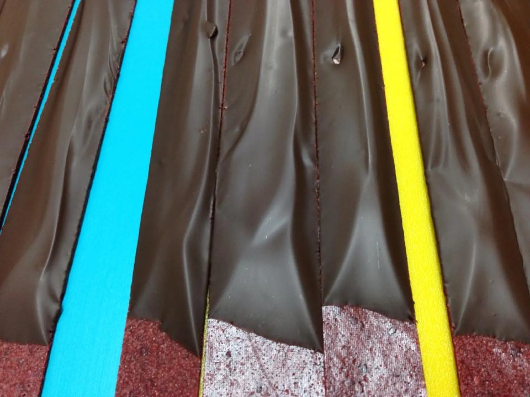 Strips of chocolate-coated fruit leather on a tray marked with blue and yellow tape.