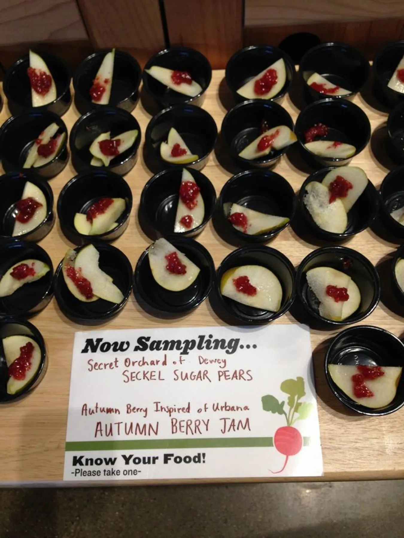 Rows of sample cups of pear with autumn berry jam behind a Now Sampling sign.