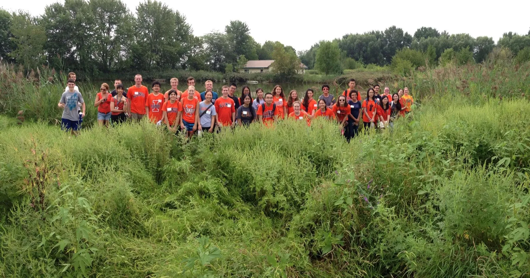 A large group of volunteers in matching orange shirts standing in a field of tall grass.