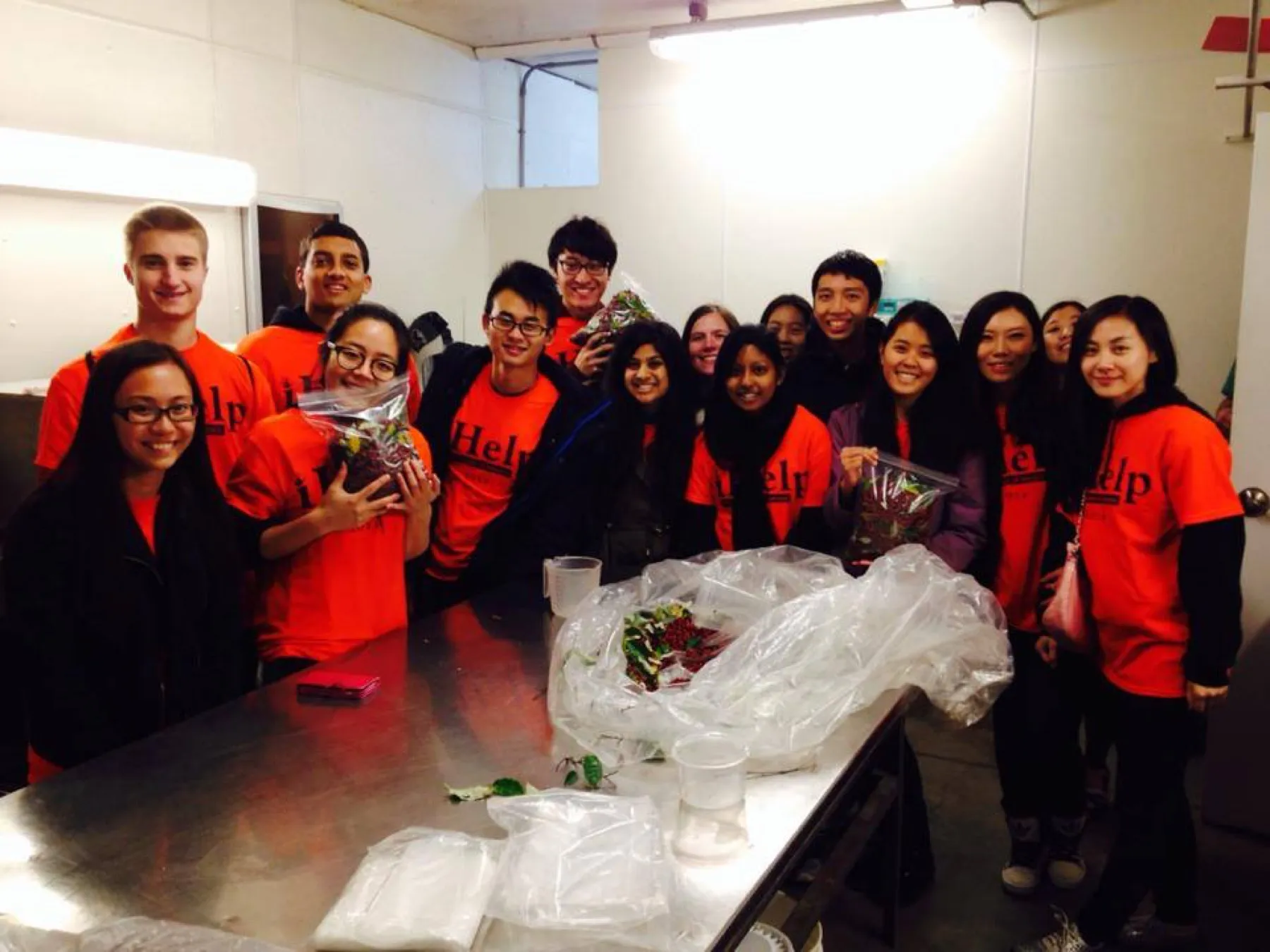 Students in orange shirts gathered around a steel table covered in bags of berries.